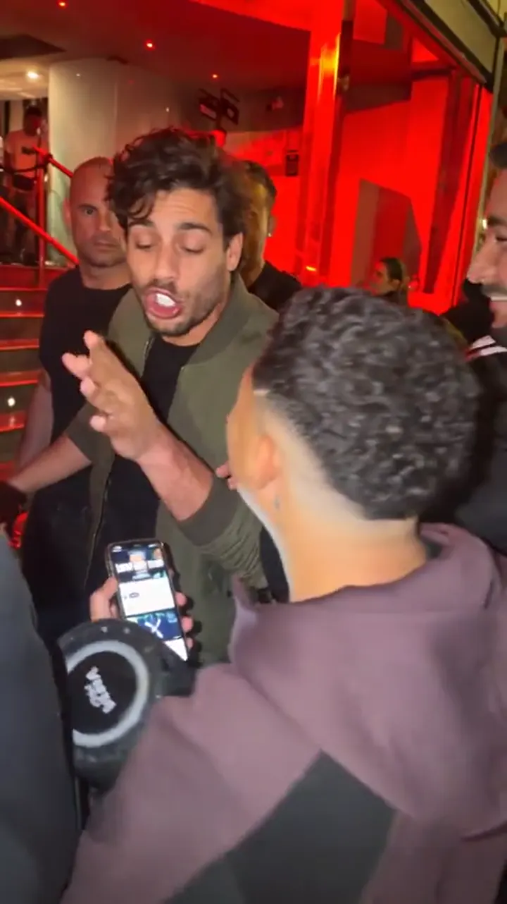 A later frame of an AI remix: an AI-generated person mid-sentence, the crowd and speaker holder unchanged